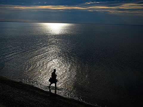 A person walks along the seashore at the Curonian Spit, a 98 kilometres long thin curved sand-dune spit that separates the Curonian Lagoon from the Baltic Sea coast near Lesnoy village, 50km north of Kaliningrad, Russia, Tuesday, Aug. 16, 2022.