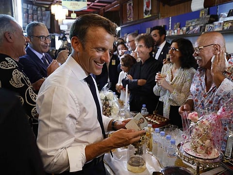 France's President Emmanuel Macron (L) reacts during his visit at the disco Maghreb Shopin, the mythical label of rai music, in front of its owner, Boualem Benhaoua (R), and France's former minister and Arab World Institute President Jack Lang (3rdR) in Oran on August 27, 2022.