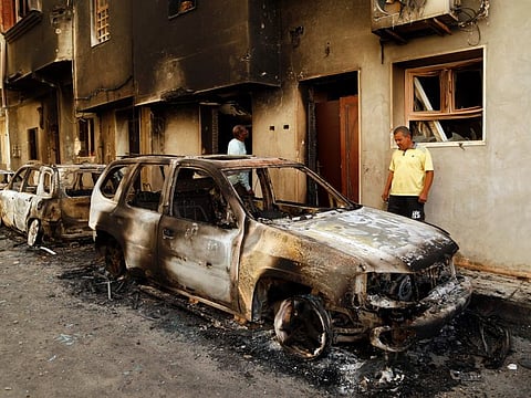 Men survey the remains of cars burned during clashes on a street in the Libyan capital of Tripoli, on August 28 2022.  