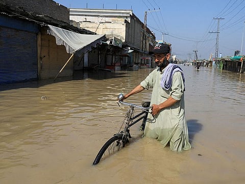 A man walks with a bicycle in flood water following rains and floods during the monsoon season in Nowshera, Pakistan