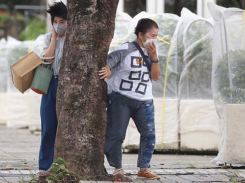 Pedestrians hold a tree to protect themselves from strong winds as Typhoon Hinnamnor hits Naha, Okinawa prefecture, Japan Sunday, Sept. 4, 2022. 