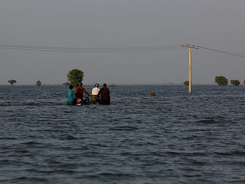 Men walk with their motorcycles amid flood water, following rains and floods during the monsoon season in Bajara village, at the banks of Manchar lake, in Sehwan on September 6, 2022.  