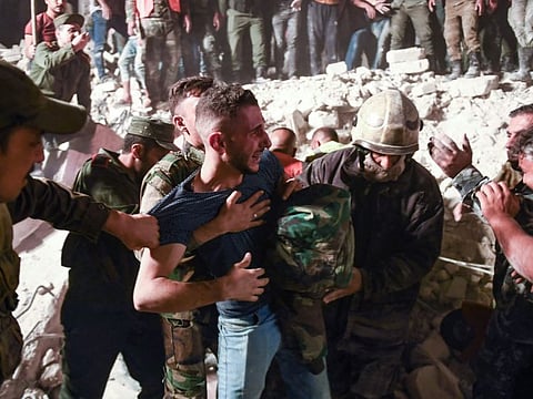 A man is restrained as rescuers search for victims and survivors amidst the rubble of a building that collapsed in Syria's northern city of Aleppo, on September 7, 2022.  