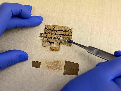 An Israel Antiquities Authority conservator inspects a papyrus fragment presented by the IAA at its Dead Sea conservation lab in Jerusalem on September 7, 2022.
