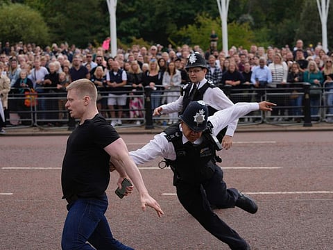 Police officers chase a man as he runs over barrier before King Charles III arriving to Buckingham Palace in London, on September 10, 2022. 