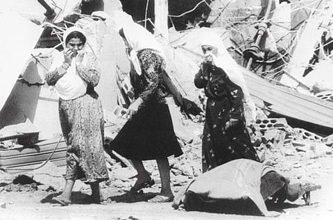 In this file photo taken on September 19, 1982, women pass by the corpse of a Palestinian killed in a two-day massacre by Christian militiamen at the refugee camps of Sabra and Shatila in Lebanon's capital Beirut.  