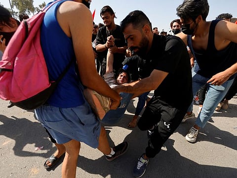 A protester affected by tear gas is carried during clashes with Iraqi security forces at a gathering marking the third anniversary of the anti-government protests in Baghdad on October 1, 2022.  