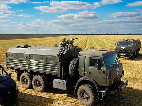 During a trip organized by the Russian Ministry of Defense, a Russian soldier stands guard atop a military truck as foreign journalists observe farmers at the Voznesenka-Agro farm harvest grain in a field near Melitopol, southern Ukraine, on Thursday, July 14, 2022.