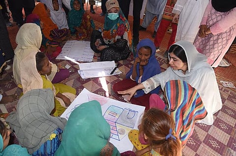 This handout picture taken and released by Chief Minister House Office of Sindh Province on October 12, 2022 shows Yousafzai (right) speaking with flood-affected children at a makeshift school in Johi, Dadu district of Sindh province.  