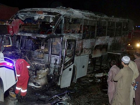 Volunteers gather beside a charred bus on a highway in Nooriabad, Pakistan, on Oct. 13, 2022.  
