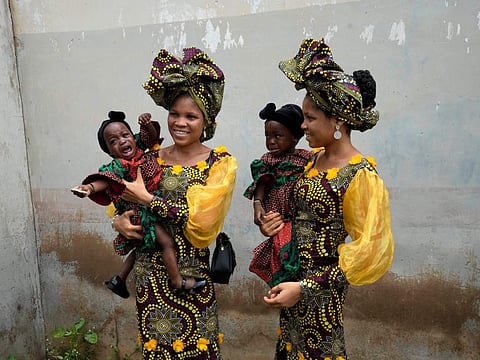 Twins Oladapo Taiwo, left, and Oladapo Kehinde, 21, pose for photographs holding relative's twins during the annual twins festival in Igbo-Ora South west Nigeria, Saturday, Oct. 8, 2022.