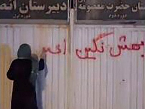  This image grab taken from a UGC video posted on October 17, 2022 show a woman writing graffiti on the wall of a girls’ school in the northern Iranian city of Zanjan reading in Farsi: “Dont call these protests, this is a revolution.”  