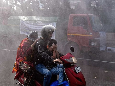People move past a Mobile Anti-Smog Gun vehicle spraying water to control pollution after being flagged off by Delhi Environment Minister Gopal Rai, in New Delhi on Tuesday, October 25, 2022.