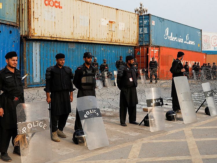 Police officers and paramilitary soldiers with riot gear stand near shipping containers used to block the area at the Red Zone, ahead of the planned true freedom march by the former Prime Minister Imran Khan to pressure the government to announce new elections, in Islamabad.