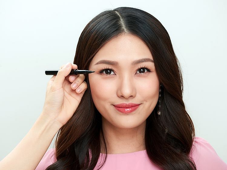 Woman in a pink t-shirt applying eyeliner