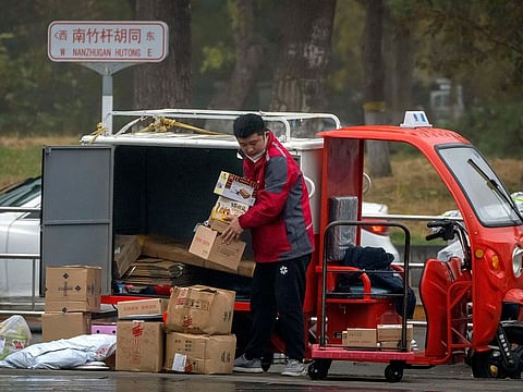 A delivery courier sorts packages along a street in Beijing.
