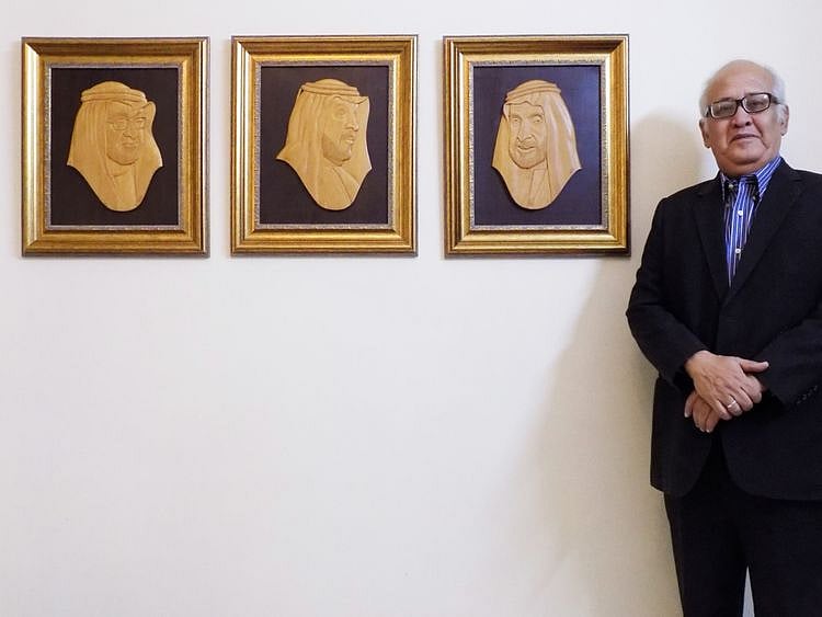 Pakistani medallion portrait artist Khalil Najmi standing alongside his wood-carved portraits o-1669909396623