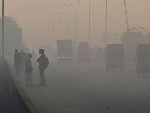 Students (left) wait for transport alongside a road amid heavy smog conditions in Lahore on December 7, 2022.  