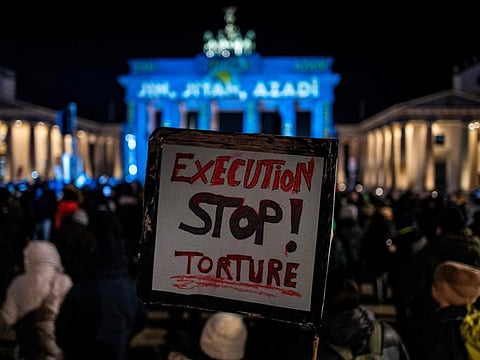 An activist displays a placard during a demonstration in support of demonstrators in Iran, in front of the Brandenburg Gate illuminated with the words "Woman, Life, Freedom" in various languages including Kurdish and Persian, in Berlin on December 13, 2022. 