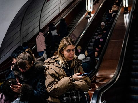 Women follow news on their mobile phones while civilians take shelter inside a metro station during an air raid alert in the centre of Kyiv on December 16, 2022.