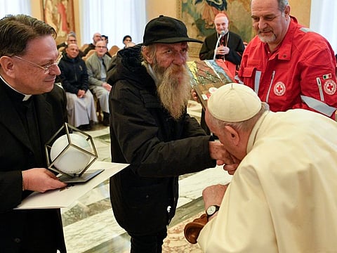 Pope Francis kisses the hand of a homeless man during his 86th birthday celebration at the Vatican on December 17, 2022.
