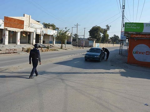A Pakistani policeman checks a car in front of a shuttered market after Taliban militants seized a police station in Bannu on December 20, 2022.