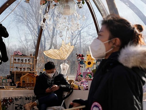 A vendor wears a mask as he waits for customers at a popup store in Beijing, Tuesday, Dec. 27, 2022.
