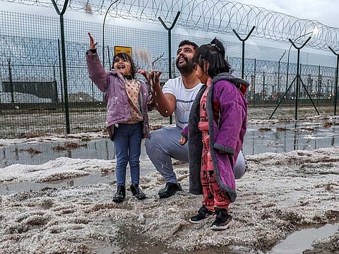 A man and children toss handfuls of hail picked up off the side of a road after a storm in the Umm al-Haiman district, about 55 kilometres south of Kuwait City, on December 27, 2022. 