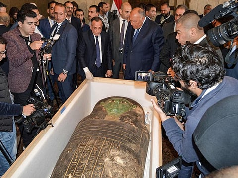 Egypt's Foreign Minister Sameh Shoukry (C-R) and the head of the Supreme Council of Antiquities Mostafa Waziri (C-L) are surrounded by journalists as they inspect an ancient Egyptian wooden sarcophagus being handed over and which was formerly displayed at Houston Museum of Natural Sciences after having been looted and smuggled years prior, at the foreign ministry headquarters in the capital Cairo on January 2, 2023.