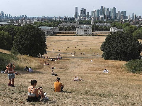 People sit on the sun-parched grass in Greenwich Park with the Maritime museum and Canary Wharf financial district in the background in London, Sunday July 17, 2022. Britain had its warmest year on record in 2022, official figures showed Thursday, Jan. 5, 2023, the latest evidence of how climate change is transforming Europe’s weather. 
