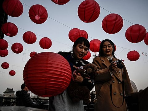 People walk past red lanterns at a rooftop cafe near the Drum Tower in Beijing on January 6, 2023.  