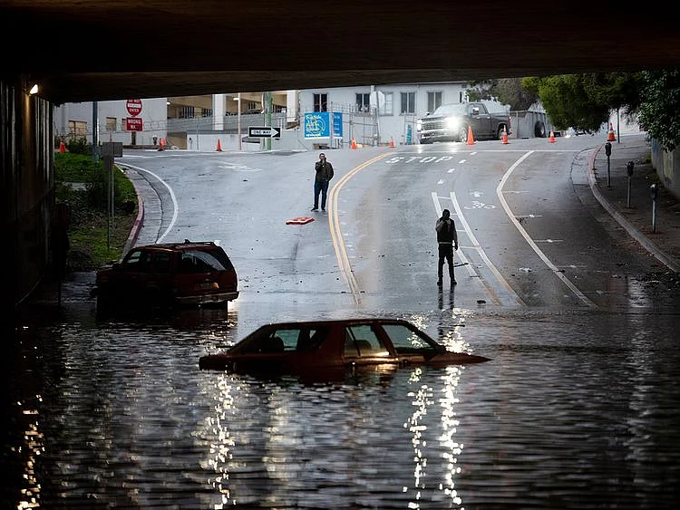 People photograph a car sitting in flooded water at an underpass in Oakland, California. 