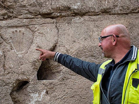 A handout picture provided by the Israel Antiquities Authority on January 25, 2023 shows a Israeli archaeologist pointing at a hand imprint that was discovered carved into a 1,000-year-old dry moat that surrounded Jerusalems Old City during excavations of defencive fortifications. 