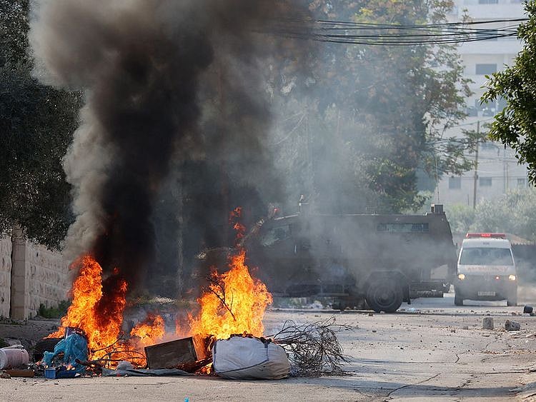  An ambulance drives past an Israeli military vehicle as smoke rises from objects set on fire by Palestinian demonstrators, in Jenin, on January 26, 2023.  