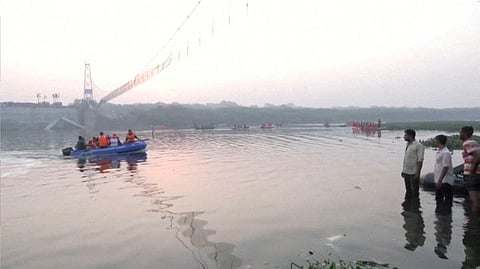 People look on as rescuers in boats work at the site of a suspension bridge collapse in Morbi town in Gujarat on October 31, 2022. 