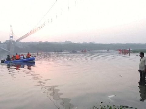 People look on as rescuers in boats work at the site of a suspension bridge collapse in Morbi town in Gujarat on October 31, 2022. 