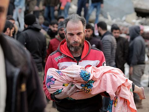 A Syrian man carries the body of a child on February 7, 2023, in the town of Jandairis, in the rebel-held part of Aleppo province, as search and rescue operations continue following a deadly earthquake. 