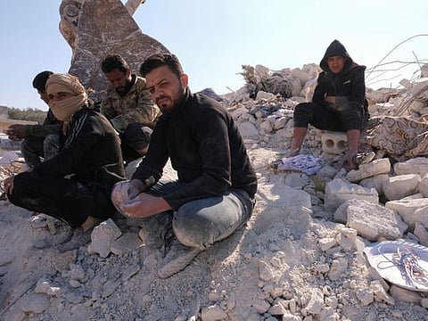 Men with hands covered in dust from sifting through rubble, sit atop ruins in the aftermath of an earthquake in the rebel-held town of Harem, in Idlib governorate, Syria, February 14, 2023