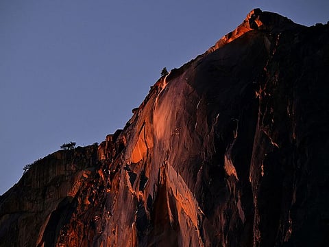 Water flowing off Horsetail Fall glows orange while backlit from the setting sun during the "Firefall" phenomenon in Yosemite National Park.