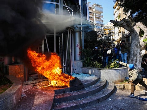A protester throws a brick at a bank after setting fire to tyres during a demonstration in Beirut on February 16, 2023.  