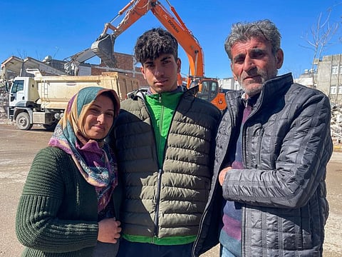 Taha Erdem, 17, his mother Zeliha Erdem, and father Ali Erdem pose for a photograph next to the destroyed building where Tahan was trapped after the earthquake of February 6, in Adiyaman, Turkey,  on Feb. 17, 2023. 