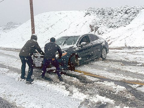 Local residents attempt to stop a car from sliding down an icy road during a snow storm in Rancho Cucamonga, California.