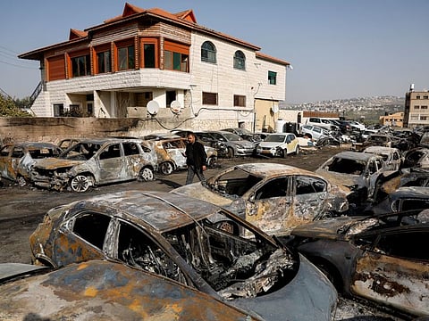 A man walks among cars burnt in an attack by Israeli settlers, following an incident where a Palestinian gunman killed two Israeli settlers, near Hawara in the West Bank, on February 27, 2023.  