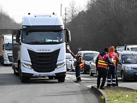 French Trade Unionists (R) give out flyers to drivers during a "filtering operation" to announce actions for a nationwide strike planned for March 7, 2023, at the Regional Transport Centre of Lesquin, near Lille, on March 6, 2023.