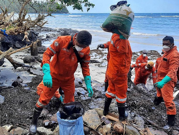 Coast guard personnel and volunteers collecting debris covered with oil