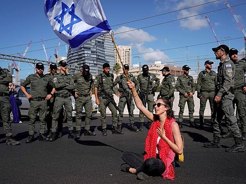 A demonstrator waves the Israeli flag seated on a highway while flanked by paramilitary border police during a protest against plans by Prime Minister Benjamin Netanyahu's government to overhaul the judicial system, in Tel Aviv, on Thursday, March 9, 2023.  