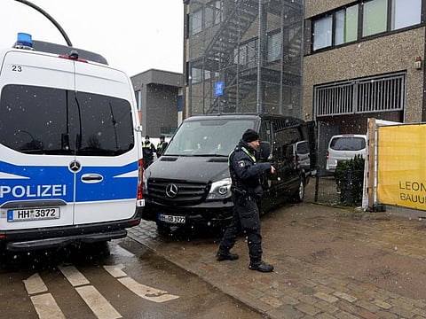 A police officer walks next to a police vehicle and an undertakers' vehicle outside a building housing a Kingdom Hall of Jehovah's Witnesses after a deadly shooting, in Hamburg, northern Germany, March 10, 2023.  