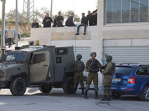 Palestinian youths watch as Israeli soldiers take position near the Jit junction west of Nablus during an army operation in the occupied northern West Bank on March 12, 2023. 