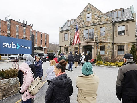 Customers wait in line outside a branch of the Silicon Valley Bank (SVB) in Wellesley, Massachusetts, on March 13, 2023.     