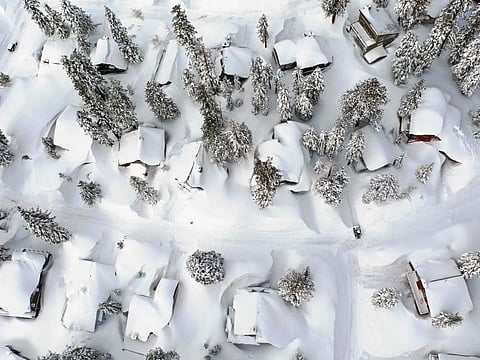 In an aerial view, snow covers roofs next to snowbanks piled up from new and past storms in the Sierra Nevada mountains, in the wake of an atmospheric river event, on March 12, 2023 in Mammoth Lakes, California.